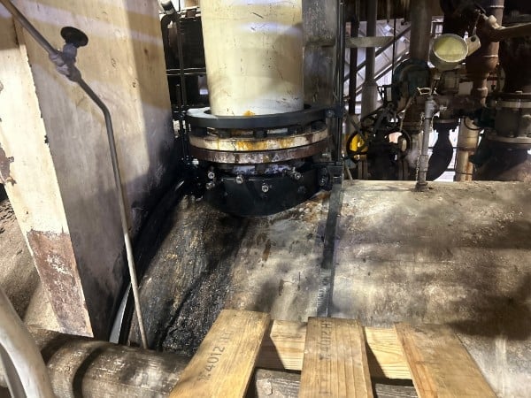 Industrial machinery with large circular metal component in warehouse or factory setting with concrete floor and wooden pallets