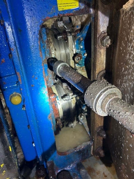 Close-up of industrial machinery with blue metal housing, metal shaft, and mechanical components covered in dust and condensation